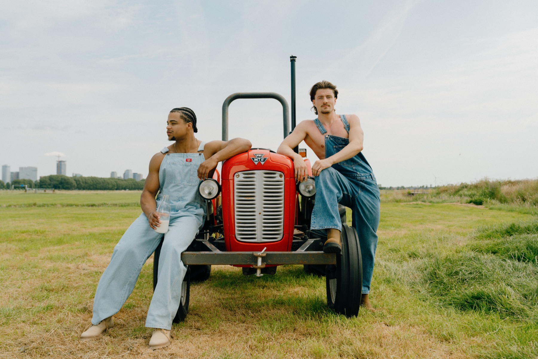Twee sporters in overalls leunen tegen een rode vintage tractor in een weiland